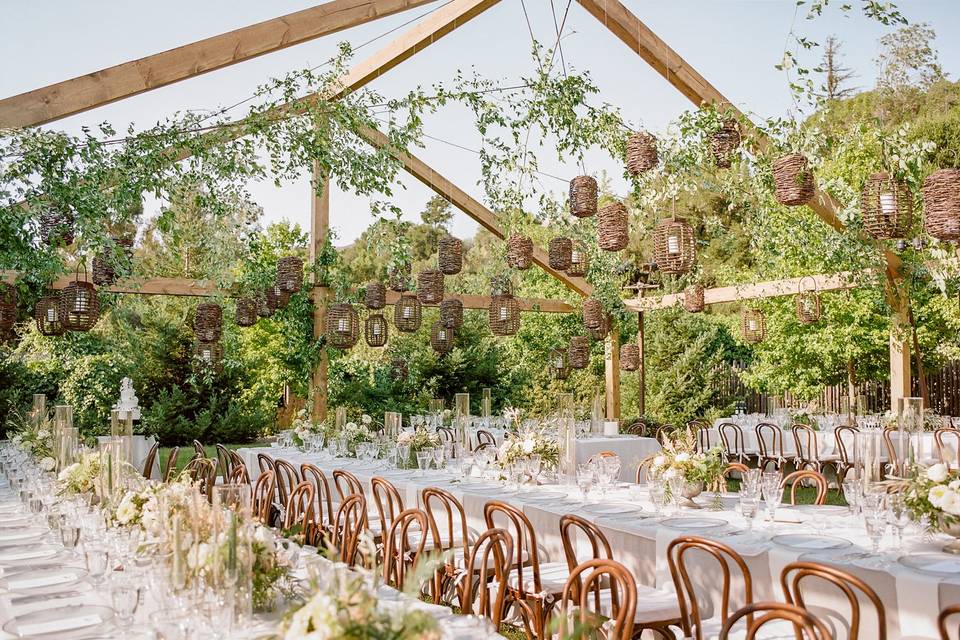 Large outdoor wedding reception dinner at Gardener Ranch in Carmel Valley under a wooden pergola strung with rattan lanterns