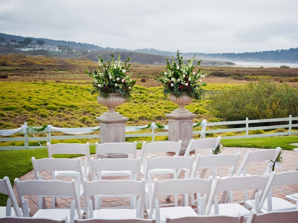 Large floral urn arrangements and white chairs set up on the Mission Ranch Inn lawn for an outdoor wedding